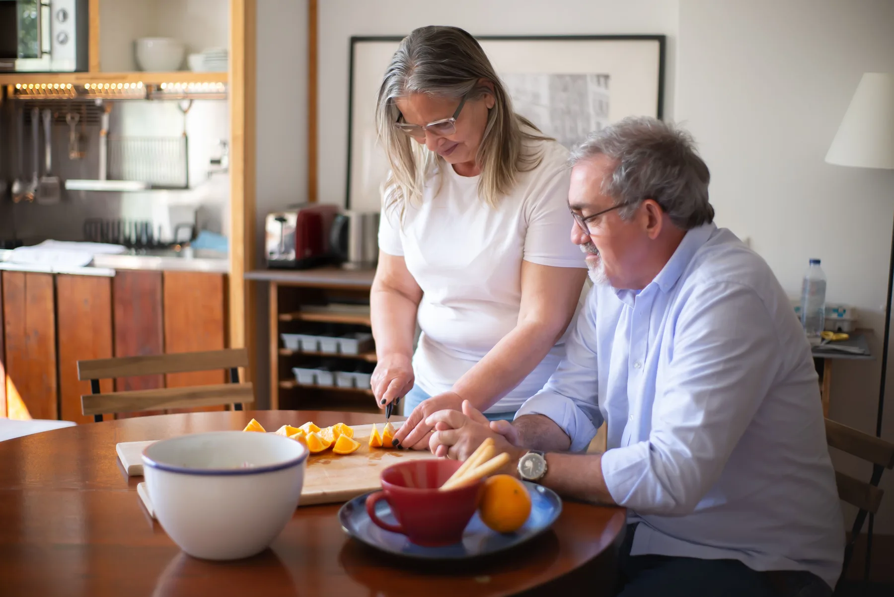 An older couple cut oranges together at a kitchen table