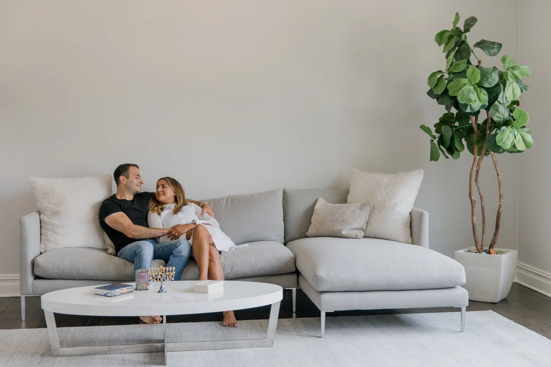 A couple sit cuddled together on a sofa in a bright living room