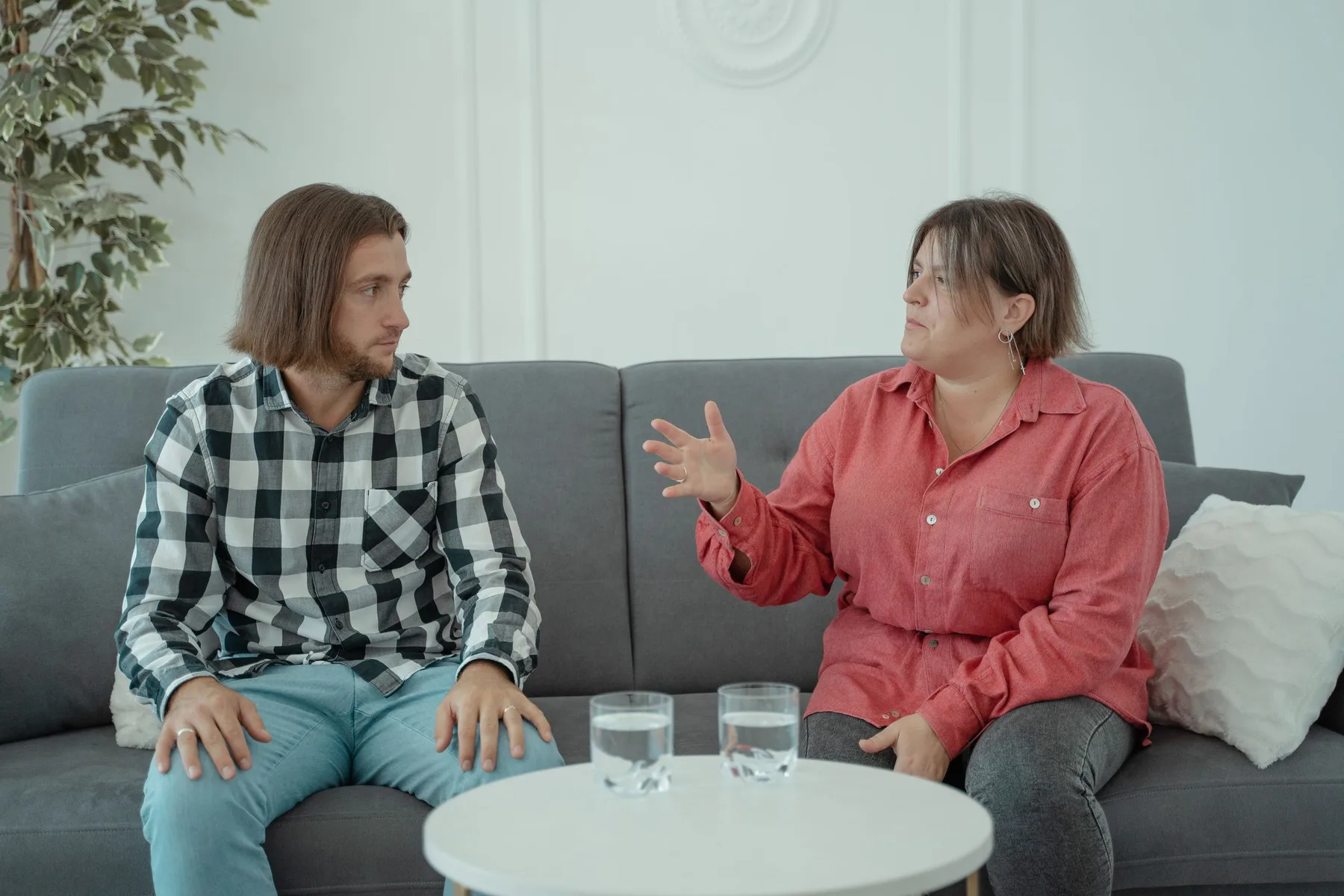 A couple sit on a sofa talking in a calm home setting.